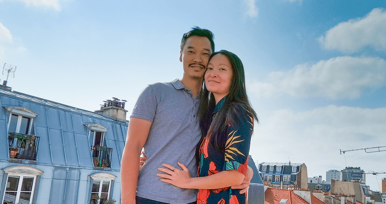 Carène and You-Liang standing together in Paris. Carène is wearing a patterned dress and You-Liang is wearing a striped blue t-shirt.