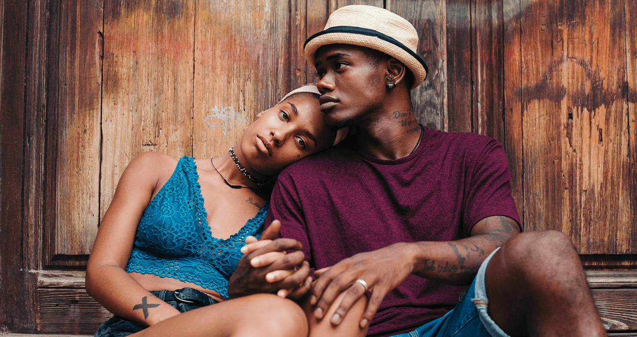 Black couple sitting together outside a house. The woman is leaning her head on her partner's shoulder.